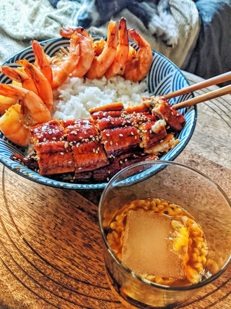 A bowl of white rice with roasted shrimp and bbq eel with passionfruit cocktail on the side.